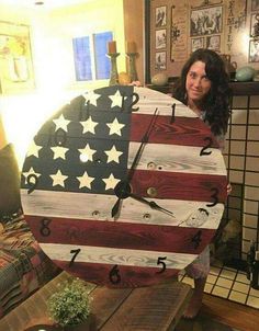 a woman standing next to a wooden clock with an american flag design on the face