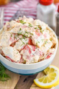 a close up of a bowl of food on a table with lemons and dill