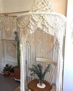 a white macrame hanging from the ceiling next to a chair and potted plant