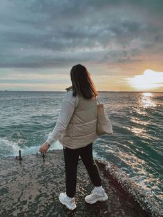 a woman standing on the edge of a cliff looking out at the ocean with her back to the camera