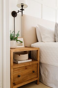 a bed with white sheets and pillows next to a wooden night stand on top of a carpeted floor