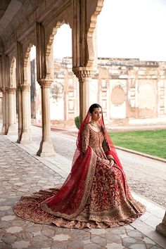 a woman in a red and gold bridal gown sitting on a stone walkway next to an archway