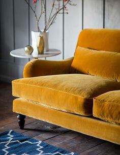 a yellow couch sitting on top of a wooden floor next to a vase filled with flowers