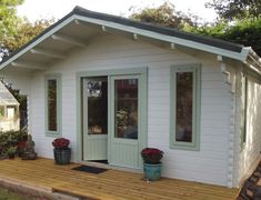 a small white shed with two plants on the porch and one door open to let in light