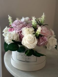 a white hat with pink and white flowers in it sitting on top of a table