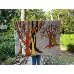 a woman holding up a piece of art made out of fabric with trees on it