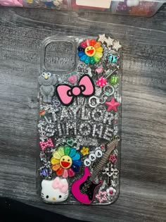 an iphone case with hello kitty and other items on it, sitting on a wooden surface