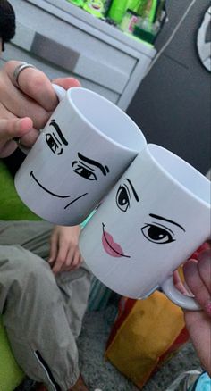 two coffee mugs with faces drawn on them being held by someone's hand