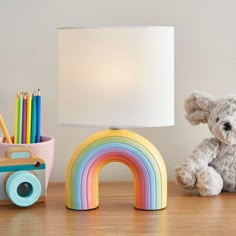 a white teddy bear sitting next to a lamp on a table with a rainbow decoration