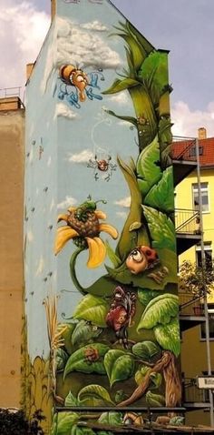 a large building painted with many different animals and plants on it's side in front of some buildings