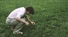 a man kneeling down in the grass picking something