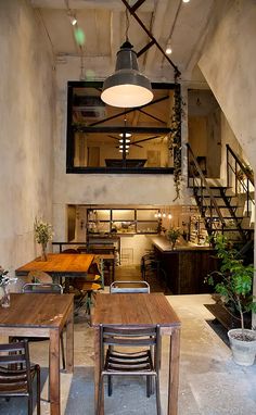 an industrial style kitchen and dining area with wooden tables, chairs, and stairs leading up to the second floor