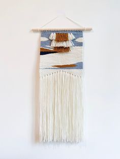 a white wall hanging with fringes on the bottom and brown, tan, and blue colors