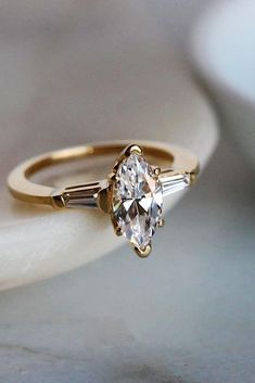 an engagement ring with three stones on it and a gold band around the band, sitting on a marble surface