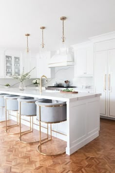 a kitchen with white cabinets and marble counter tops, gold bar stools on the island