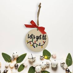 a christmas ornament hanging from a string with lights and leaves around it that says let's get at