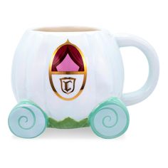 a white coffee mug with green wheels and a pink princess tiara on it's face