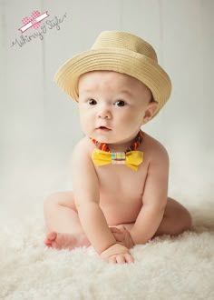 a baby wearing a straw hat and yellow bow tie sitting on a white rug in front of a wall