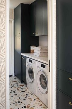 a washer and dryer in a small laundry room with black cabinetry, patterned flooring and white walls