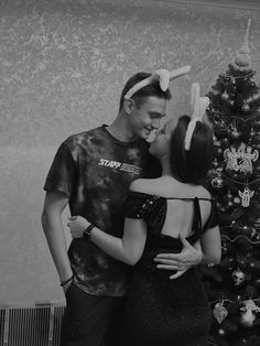 a man and woman standing in front of a christmas tree with their arms around each other