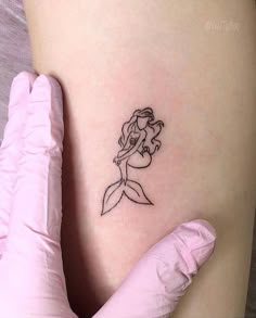 a little mermaid tattoo on the side of a woman's thigh, with her arm behind her back