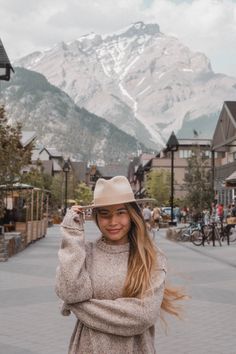 a woman standing in the middle of a street with mountains in the backgroud