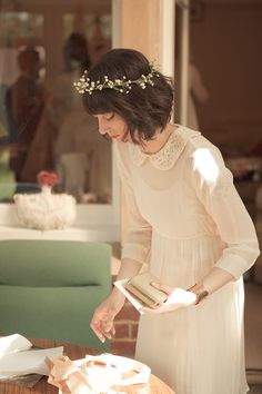 a woman in a white dress is holding a box and looking at something on the table