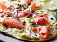 a pizza topped with salmon and onions on top of a plate next to lemon wedges