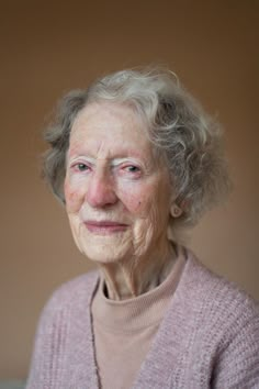 an older woman with gray hair and blue eyes wearing a pink sweater looking at the camera