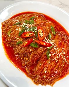 a white plate topped with spaghetti and sauce on top of a marble countertop covered in sesame seeds