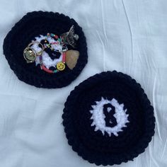 two black crocheted coasters with white letters and buttons on them, sitting on a bed