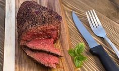 a piece of steak on a cutting board with a knife and fork next to it