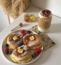 pancakes with butter and berries on a plate next to a cup of coffee, honey shake