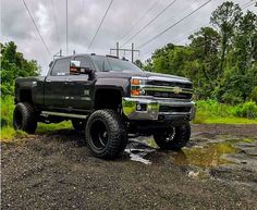 a large black truck parked on top of a dirt road next to trees and power lines