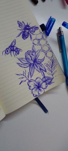 an open notebook with blue flowers and bees on it, surrounded by crayons