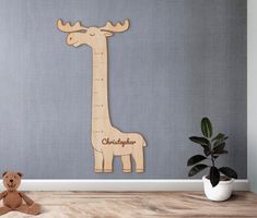 a wooden giraffe height chart next to a potted plant and stuffed animal