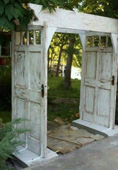 an old white wooden gate with two doors open in the middle of a garden area