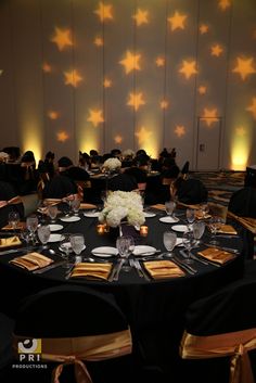 a large banquet room with black tables and gold napkins on the table are decorated with star shaped lights