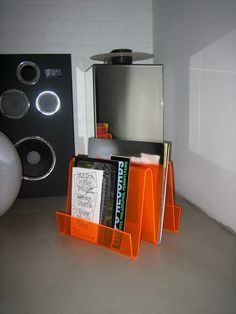 an orange book holder sitting on top of a floor next to speakers and a wall mounted speaker