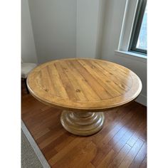 a round wooden table sitting on top of a hard wood floor next to a window