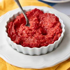 a white bowl filled with red sauce sitting on top of a table next to a yellow napkin