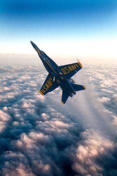 a blue and yellow fighter jet flying through the sky above some fluffy white cloud formations