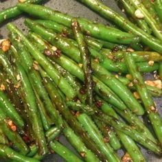 some green beans are being cooked in a pan with peanuts on the side and sauce drizzled over them