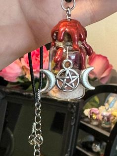 a hand holding a glass bottle with an inverted pentagramil on it and a crescent moon charm hanging from the bottom