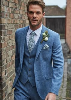 a man in a blue suit and flowered boutonniere standing next to a brick wall