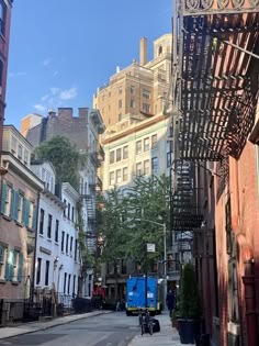 a city street with lots of tall buildings on both sides and a blue truck in the middle