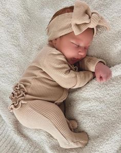 a baby sleeping on top of a white blanket wearing a headband with a bow