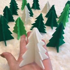 someone is holding out their hand in front of small christmas trees that have been made from paper