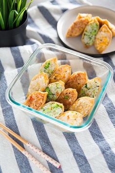 some food is in a glass dish on a striped tablecloth with chopsticks