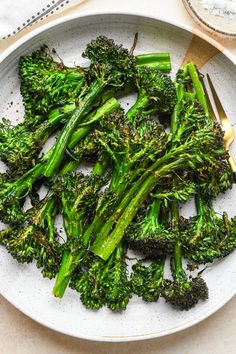 a white plate topped with cooked broccoli on top of a table next to a knife and fork